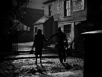 Movie still from “In Which We Serve” (1942), directed by Noël Coward – Two people holding hands while walking down a street; Wide shot, High angle