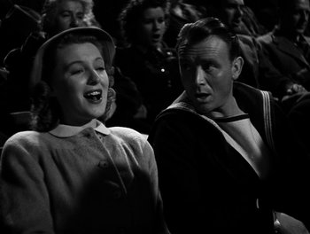 Movie still from “In Which We Serve” (1942), directed by Noël Coward – A man and a woman are standing in front of a group of people; Medium shot, Low angle