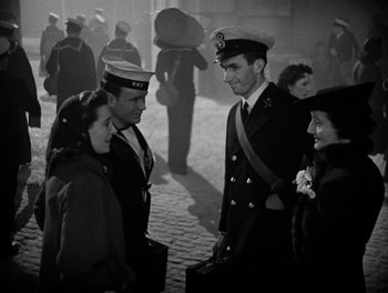 Movie still from “In Which We Serve” (1942), directed by Noël Coward – A group of people standing next to each other on a street; Medium shot, High angle