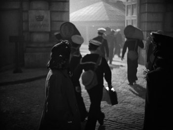 Movie still from “In Which We Serve” (1942), directed by Noël Coward – A black and white photo of a group of people walking down a street; Wide shot, High angle