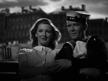 Movie still from “In Which We Serve” (1942), directed by Noël Coward – A man and a woman standing next to each other in front of a building; Medium shot, Low angle