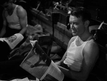 Movie still from “In Which We Serve” (1942), directed by Noël Coward – A black and white photo of a man reading a newspaper; Medium shot, Over the shoulder angle
