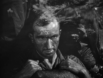 Movie still from “In Which We Serve” (1942), directed by Noël Coward – Black and white photograph of a man in the mud; Close Up shot, High angle