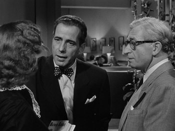 Movie still from “In a Lonely Place” (1950), directed by Nicholas Ray – A man in a suit talking to two other men; Medium shot, Over the shoulder angle