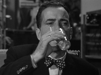 Movie still from “In a Lonely Place” (1950), directed by Nicholas Ray – A black and white photo of a man drinking a glass of wine; Close Up shot, Low angle