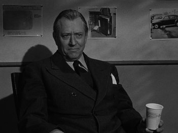 Movie still from “In a Lonely Place” (1950), directed by Nicholas Ray – An older man in a suit and tie sitting next to a cup; Medium shot, Over the shoulder angle