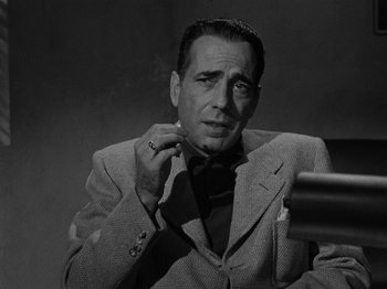 Movie still from “In a Lonely Place” (1950), directed by Nicholas Ray – A black and white photo of a man wearing a suit and tie; Close Up shot, Low angle