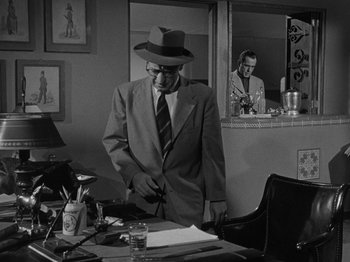 Movie still from “In a Lonely Place” (1950), directed by Nicholas Ray – An older man wearing a suit and hat standing in front of a desk; Medium shot, Over the shoulder angle
