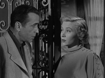 Movie still from “In a Lonely Place” (1950), directed by Nicholas Ray – A man and a woman standing next to each other in front of an iron gate; Close Up shot, Low angle