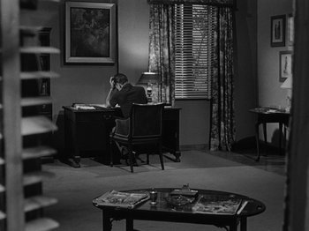 Movie still from “In a Lonely Place” (1950), directed by Nicholas Ray – A man sitting at a desk in a room; Wide shot, High angle