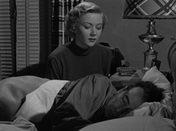 Movie still from “In a Lonely Place” (1950), directed by Nicholas Ray – A woman sitting on a bed next to a sleeping man; Medium shot, High angle