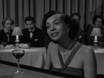Movie still from “In a Lonely Place” (1950), directed by Nicholas Ray – A woman sitting at a table in front of a glass of wine; Close Up shot, Over the shoulder angle