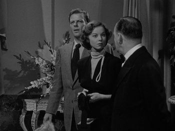 Movie still from “In a Lonely Place” (1950), directed by Nicholas Ray – A man and a woman standing next to each other in front of another man; Medium shot, Over the shoulder angle