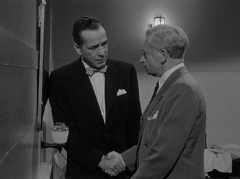 Movie still from “In a Lonely Place” (1950), directed by Nicholas Ray – Two men in suits shaking hands in a room; Medium shot, Over the shoulder angle