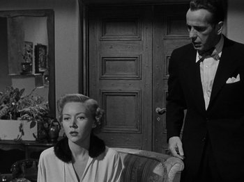 Movie still from “In a Lonely Place” (1950), directed by Nicholas Ray – A man and a woman sitting on a chair in front of a door; Medium shot, Low angle