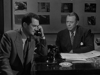 Movie still from “In a Lonely Place” (1950), directed by Nicholas Ray – Two men sitting at a table talking on the phone; Medium shot, High angle