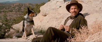 Movie still from “In a Valley of Violence” (2016), directed by Ti West – A man sitting on a rock with a dog in front of him; Medium shot, Low angle