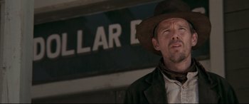 Movie still from “In a Valley of Violence” (2016), directed by Ti West – A man wearing a hat and a jacket standing in front of a building; Close Up shot, Low angle