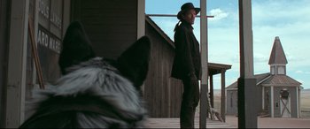 Movie still from “In a Valley of Violence” (2016), directed by Ti West – A man standing on a porch next to a dog; Medium shot, Over the shoulder angle