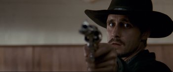 Movie still from “In a Valley of Violence” (2016), directed by Ti West – A man in a hat holding a gun in a room; Close Up shot, Low angle