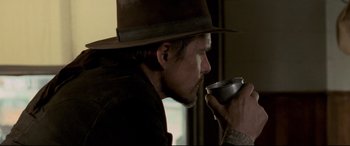 Movie still from “In a Valley of Violence” (2016), directed by Ti West – A man in a hat drinking from a metal cup; Close Up shot, Over the shoulder angle