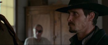 Movie still from “In a Valley of Violence” (2016), directed by Ti West – A man in a hat and sunglasses looking at another man in a hat; Close Up shot, Over the shoulder angle