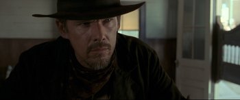 Movie still from “In a Valley of Violence” (2016), directed by Ti West – A man in a cowboy hat and a brown jacket; Close Up shot, Over the shoulder angle
