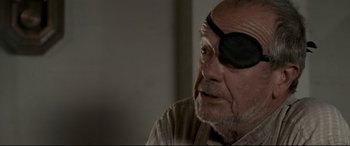 Movie still from “In a Valley of Violence” (2016), directed by Ti West – An older man wearing a eye patch and a brown shirt; Close Up shot, Over the shoulder angle