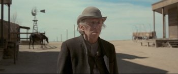 Movie still from “In a Valley of Violence” (2016), directed by Ti West – An older man wearing a hat standing in the desert; Close Up shot, Over the shoulder angle