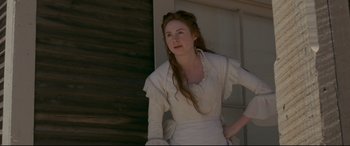 Movie still from “In a Valley of Violence” (2016), directed by Ti West – A woman in a white dress standing in front of a building; Medium shot, High angle