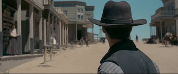 Movie still from “In a Valley of Violence” (2016), directed by Ti West – A man wearing a hat standing in front of a building; Wide shot, Over the shoulder angle