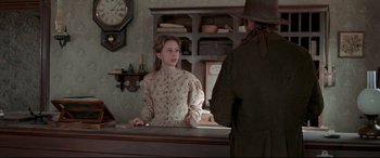 Movie still from “In a Valley of Violence” (2016), directed by Ti West – A woman in a dress and a hat standing at a counter with a man; Medium shot, Over the shoulder angle