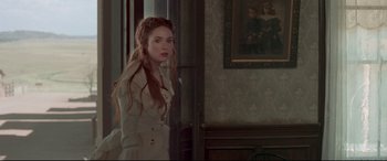 Movie still from “In a Valley of Violence” (2016), directed by Ti West – A woman in a white dress standing next to a wall; Medium shot, Over the shoulder angle