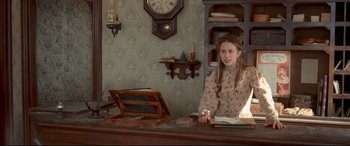 Movie still from “In a Valley of Violence” (2016), directed by Ti West – A woman sitting at a desk in front of a clock; Medium shot, High angle