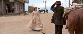 Movie still from “In a Valley of Violence” (2016), directed by Ti West – A woman in a dress standing next to a man in a cowboy hat; Wide shot, Over the shoulder angle