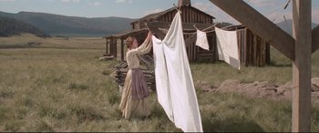 Movie still from “In a Valley of Violence” (2016), directed by Ti West – A woman hanging laundry on a clothesline outside; Wide shot, Low angle