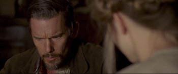 Movie still from “In a Valley of Violence” (2016), directed by Ti West – A person sitting down with another person; Close Up shot, Over the shoulder angle