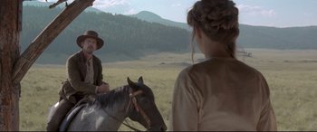Movie still from “In a Valley of Violence” (2016), directed by Ti West – A man and a woman riding a horse in a field; Medium shot, Over the shoulder angle