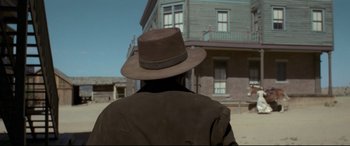 Movie still from “In a Valley of Violence” (2016), directed by Ti West – A man wearing a brown hat in front of a building; Wide shot, Low angle