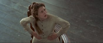 Movie still from “In a Valley of Violence” (2016), directed by Ti West – A young woman in a dress clutches her stomach; Medium shot, Low angle