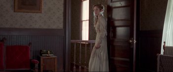 Movie still from “In a Valley of Violence” (2016), directed by Ti West – A woman in a dress standing next to a door; Wide shot, Over the shoulder angle