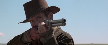 Movie still from “In a Valley of Violence” (2016), directed by Ti West – A man in a hat and a brown jacket is holding a gun; Close Up shot, Low angle