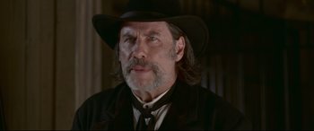 Movie still from “In a Valley of Violence” (2016), directed by Ti West – A person wearing a hat and a suit; Close Up shot, Low angle