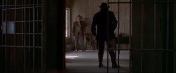 Movie still from “In a Valley of Violence” (2016), directed by Ti West – A man in a suit and a hat standing in a room with another man; Wide shot, Low angle