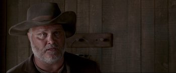 Movie still from “In a Valley of Violence” (2016), directed by Ti West – An older man wearing a cowboy hat in front of a wooden wall; Close Up shot, Low angle
