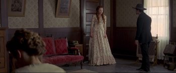 Movie still from “In a Valley of Violence” (2016), directed by Ti West – A woman in a long dress standing in front of a door; Wide shot, High angle