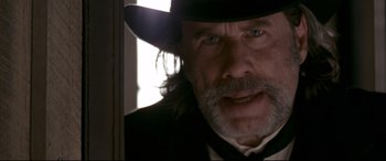 Movie still from “In a Valley of Violence” (2016), directed by Ti West – An older man wearing a black hat and a black suit; Close Up shot, Low angle