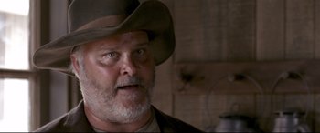 Movie still from “In a Valley of Violence” (2016), directed by Ti West – An older man wearing a cowboy hat in a room; Close Up shot, Low angle