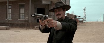 Movie still from “In a Valley of Violence” (2016), directed by Ti West – A man in a black hat is holding a gun; Medium shot, Low angle