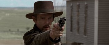 Movie still from “In a Valley of Violence” (2016), directed by Ti West – A man in a hat is pointing a gun; Close Up shot, Over the shoulder angle